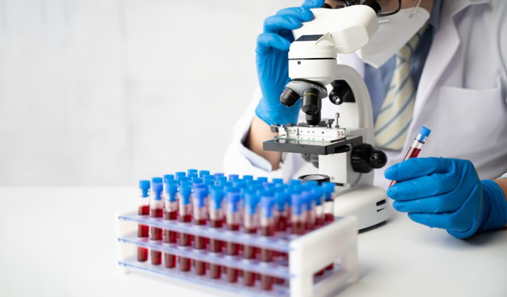 medical worker looking at blood test vials through a microscope